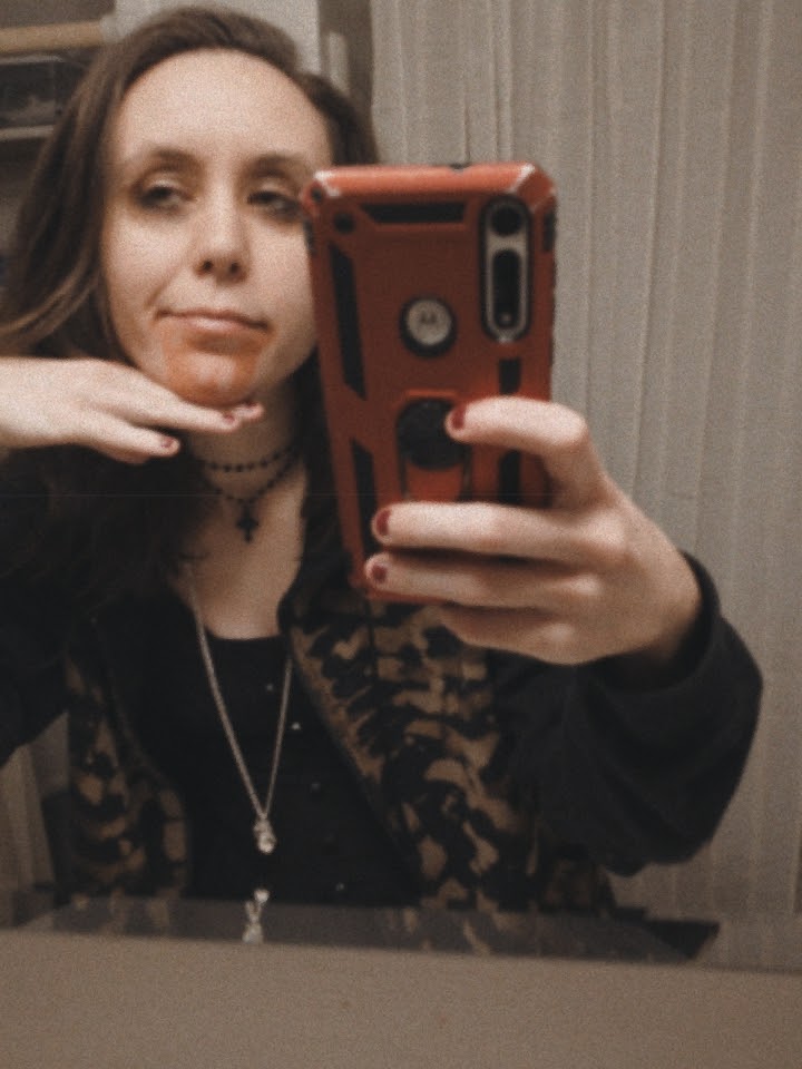 Mirror selfie of a white person with medium length brown hair, wearing a skeleton hoodie, with fake blood on their mouth
